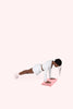 Woman performing a plank exercise on a pink folded Bala Compact Mat against a white background