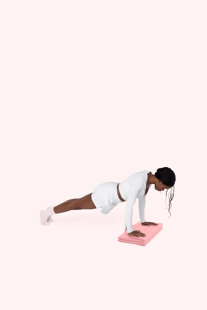 Woman performing a plank exercise on a pink folded Bala Compact Mat against a white background