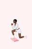 Woman in white outfit exercising on a pink Bala Compact mat against a white background
