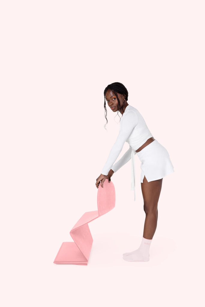 Woman holding a pink Bala Compact yoga mat on a white background