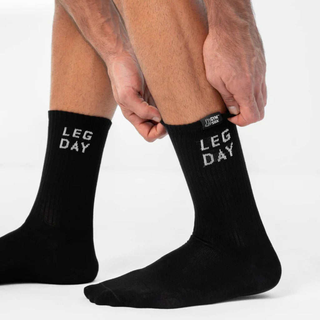 Black socks with 'LEG DAY' text worn by a person on a white background