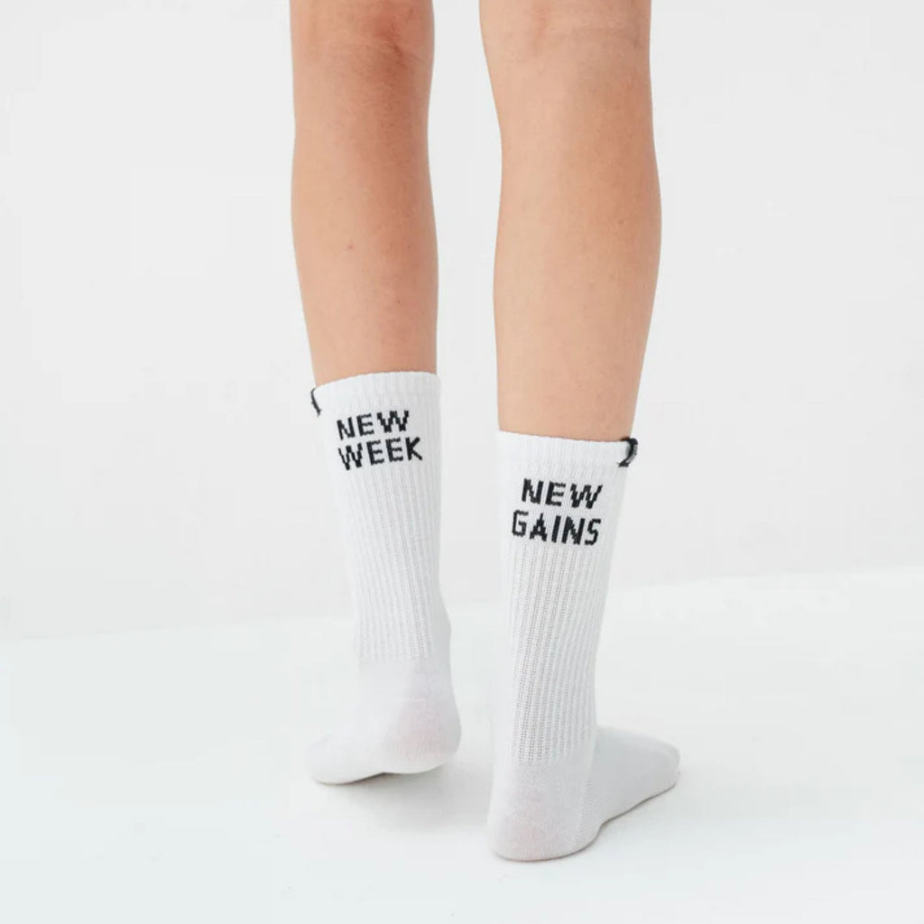White socks with 'New Week' and 'New Gains' text worn by a person on a light gray background