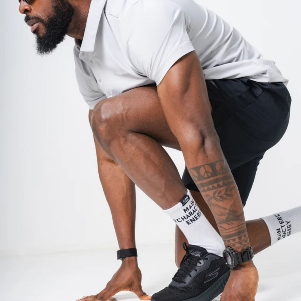 Person wearing black sneakers and white socks with text, crouching on a light background