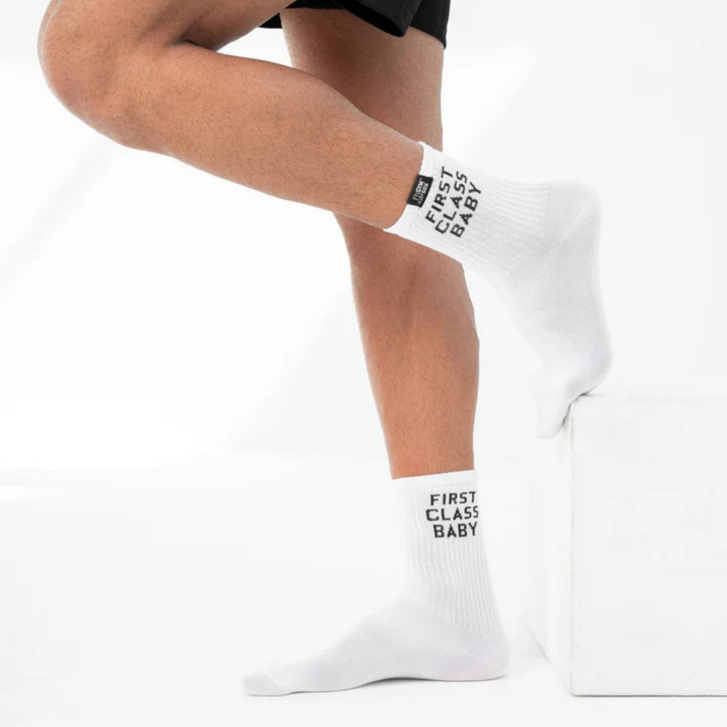 White socks with 'First Class Baby' text worn by a person on a white background
