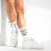 White crew socks with black text reading 'SHUT UP LEGS, YOU'RE FINE' worn with white low-top sneakers on a model's legs, shown against a bright white studio background.