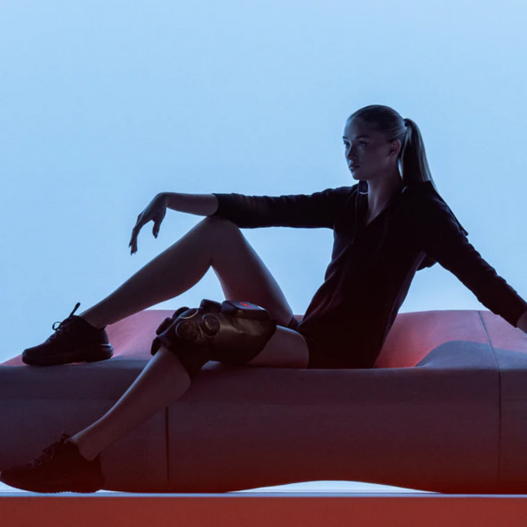 person sitting on a red couch wearing hyperice contrast knee hot and cold compression therapy to treat knee pain