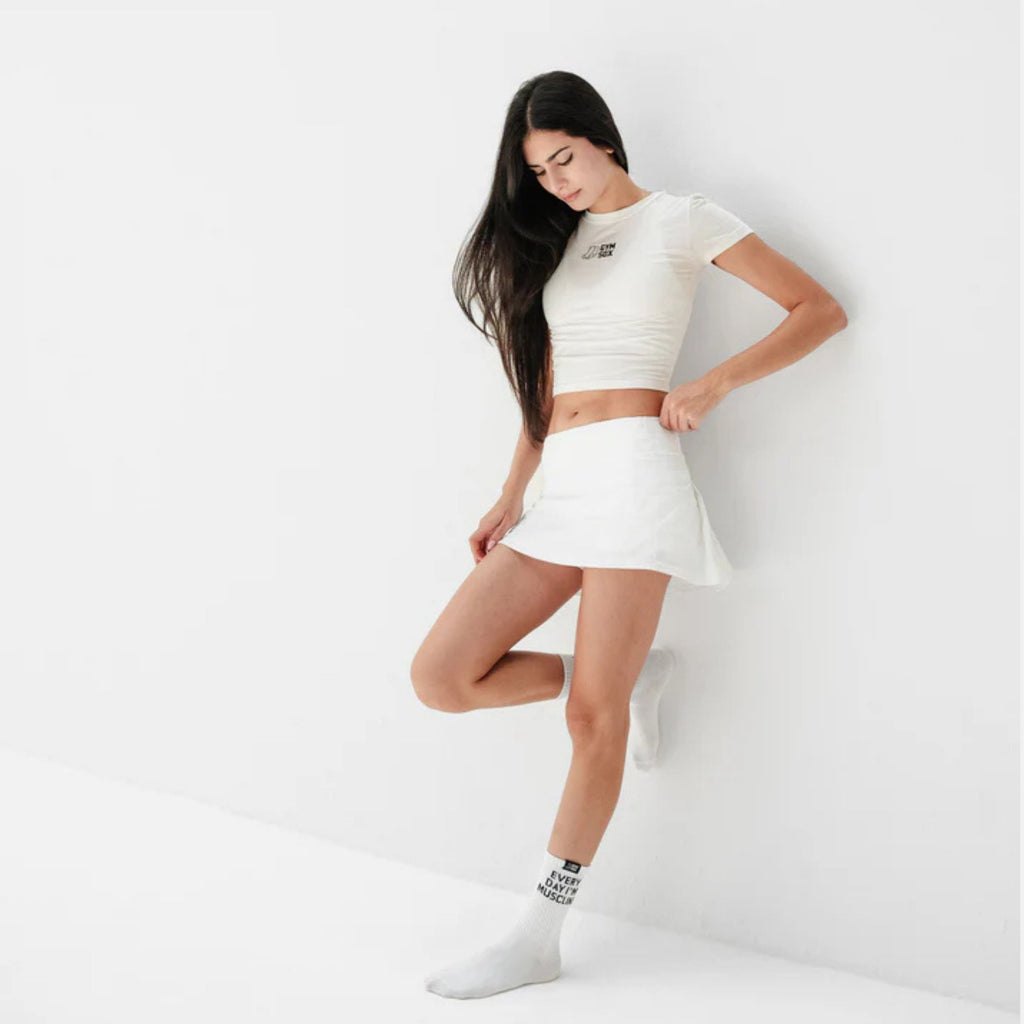 Woman wearing a white crop top and skirt with black socks on a light gray background