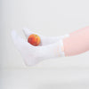 Person wearing white socks with a peach between them on a light gray background