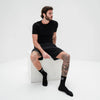 Man wearing black socks with visible branding sitting on a white cube against a white background