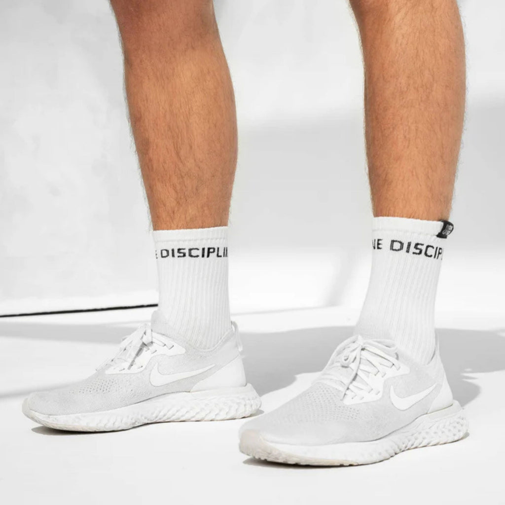 White Nike running shoes worn with white crew socks featuring black text, shown on a model's feet against a clean white background.