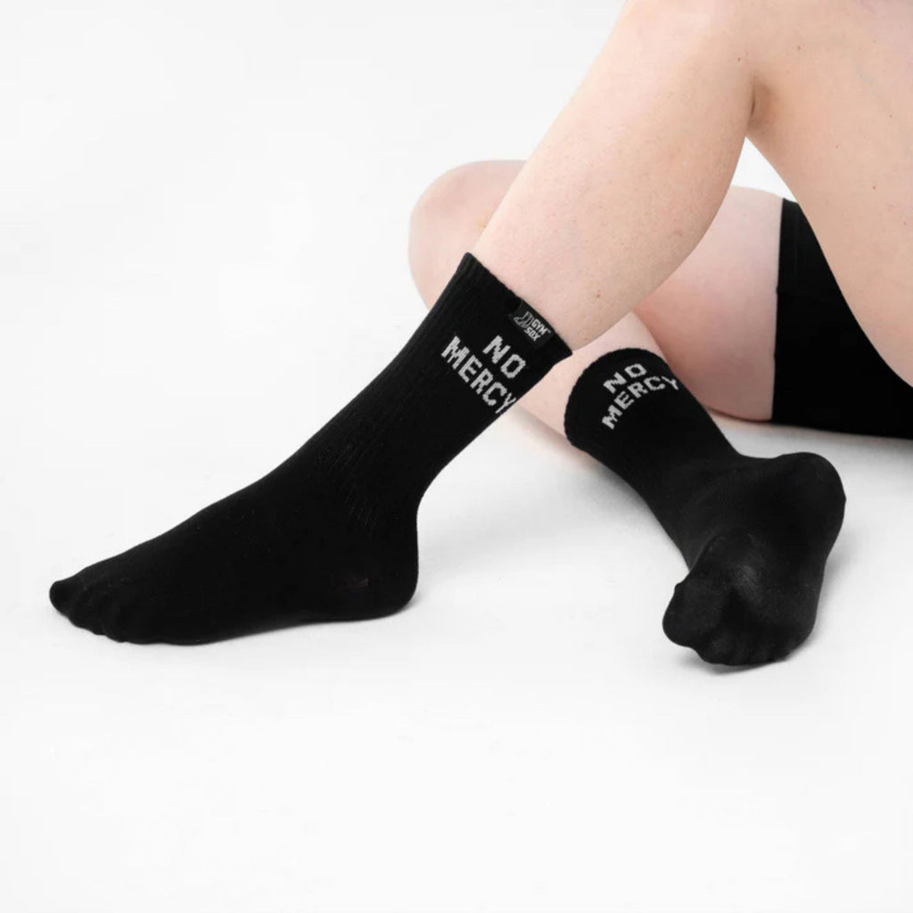 Black socks with 'NO MERCY' text worn by a person on a white background
