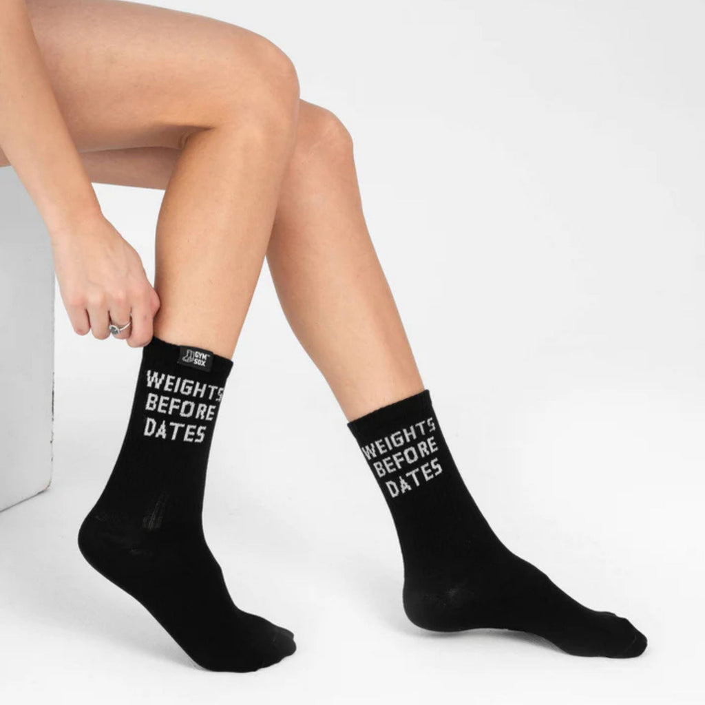 Person wearing black socks with text, sitting on a white surface.