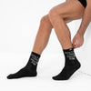 Person wearing black socks with text, sitting on a white background