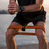 Person sitting on a beach with an orange resistance band, wearing a black watch.