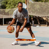 Man holding a basketball on an outdoor court with sports equipment in the background