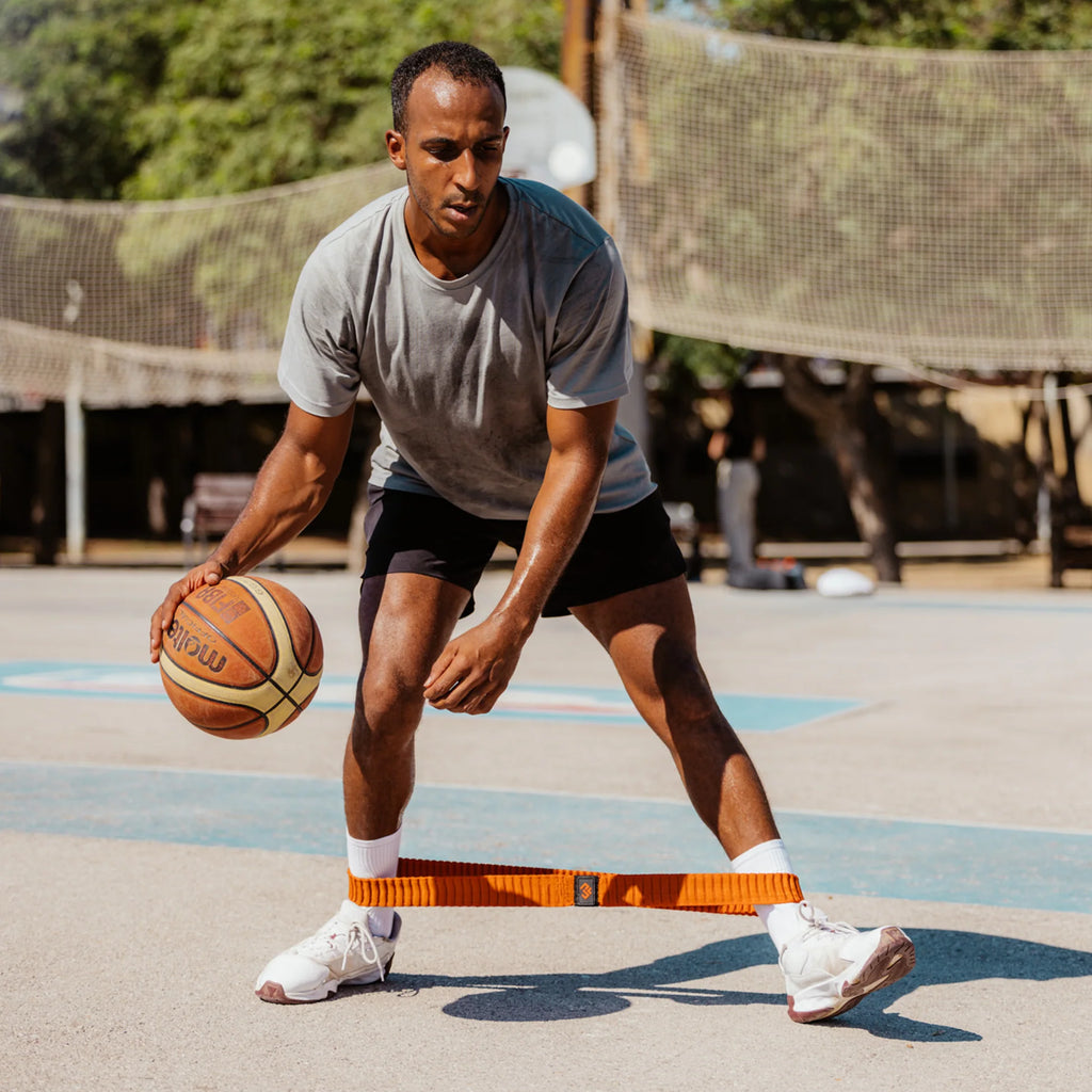 Man holding a basketball on an outdoor court with sports equipment in the background