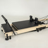 Maple and black folding Pilates reformer by FOLD, featuring adjustable foot bar and head rest.
