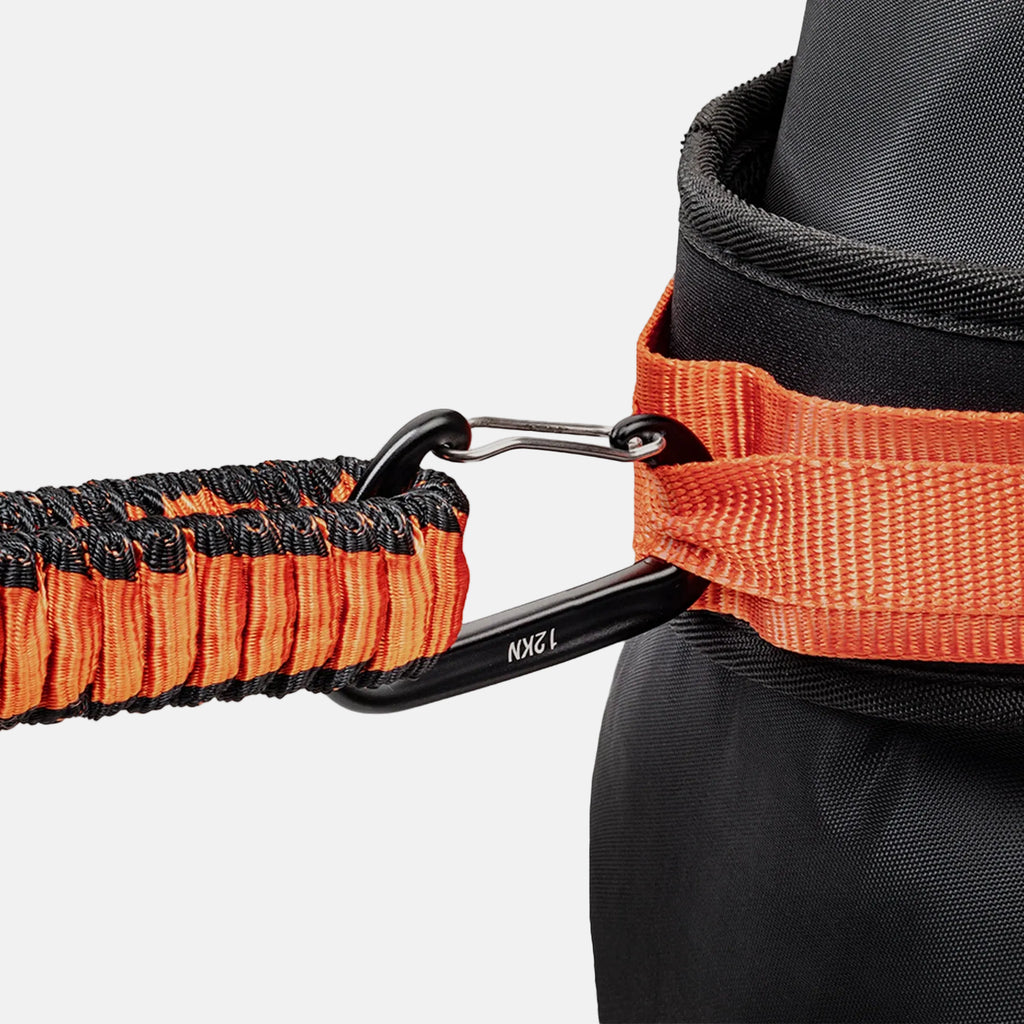 Close-up of an orange and black resistance band attached to a black belt on a light gray background