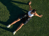 Black compression hip recovery tool by Hyperice worn on a woman lying on a grass surface with her arms outstretched.

