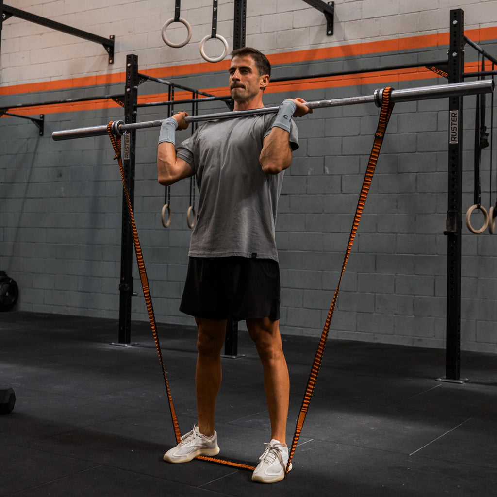 Man lifting a barbell in a gym setting with various equipment in the background.