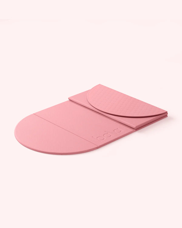 Pink colored semi-folded Bala Compact yoga mat on white background