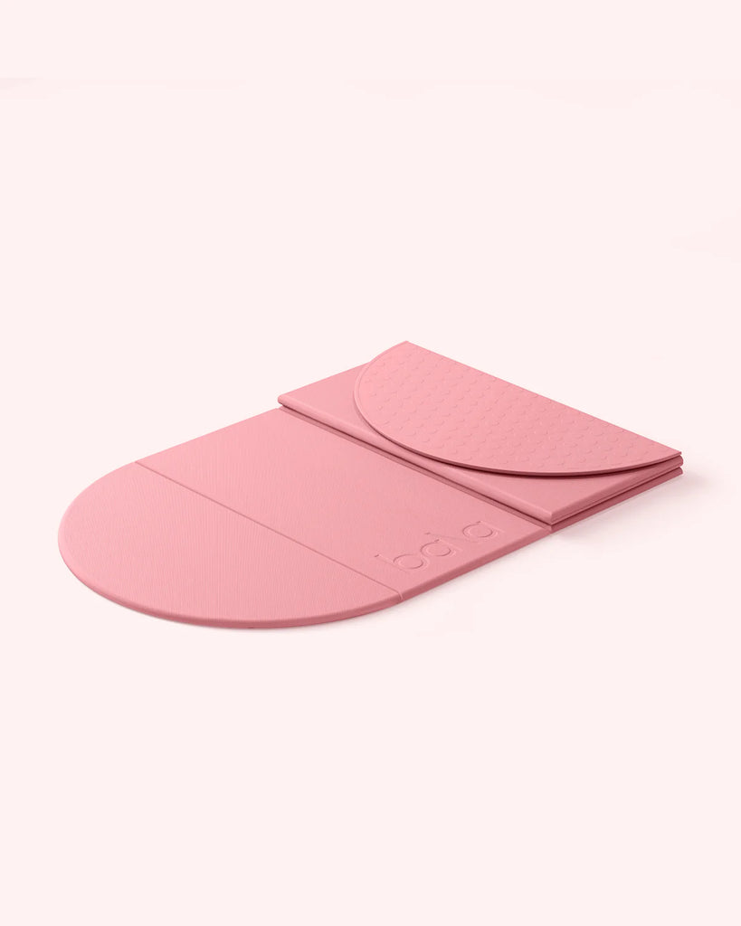 Pink colored semi-folded Bala Compact yoga mat on white background