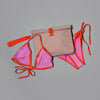 A coordinated swimwear and bag set laid flat on a gray background: a pink bikini top and matching bottoms with bright orange trim and ties, plus a beige pouch with orange trim and a flap closure.