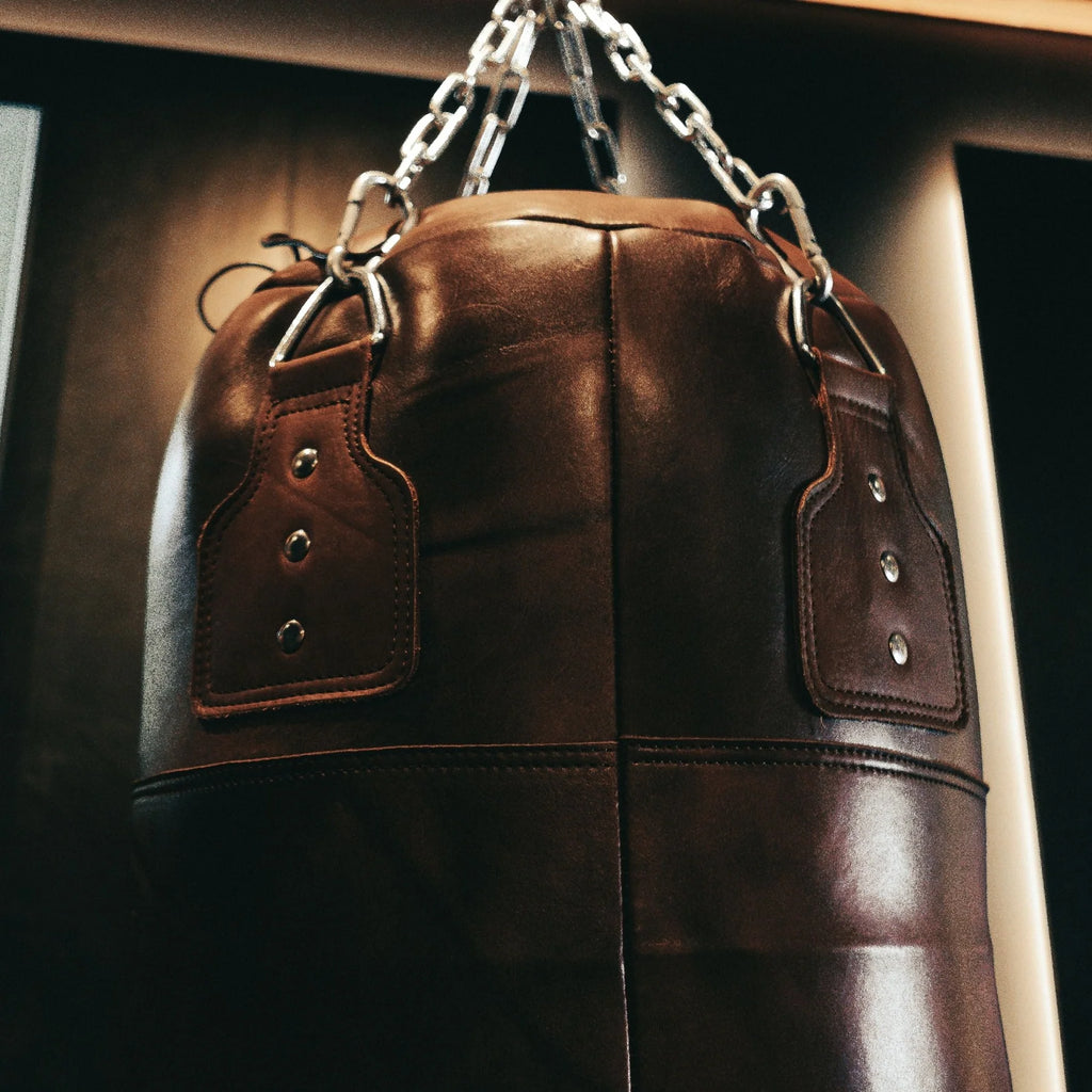 Brown leather punching bag with chain on a dark background