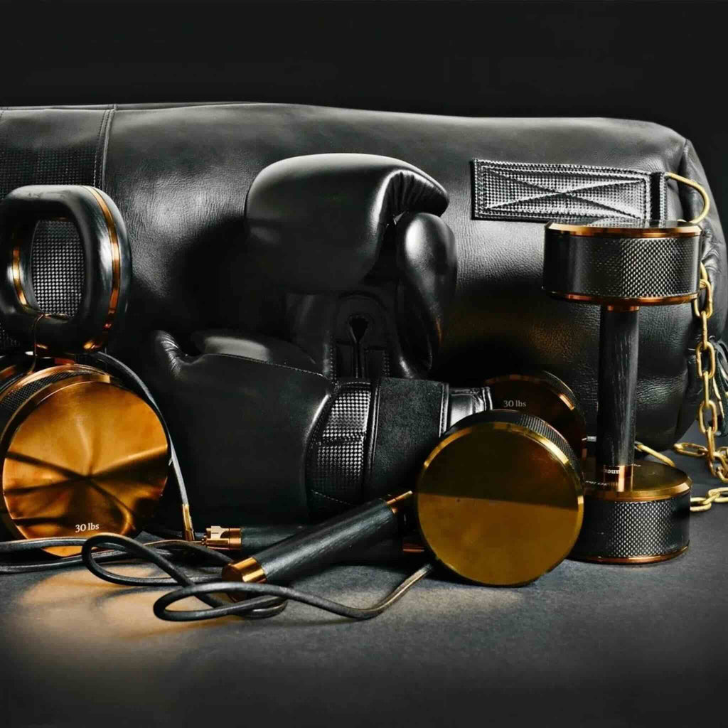 Black boxing gloves, dumbbells, skipping rope, and punching bag with gold accents on a black background