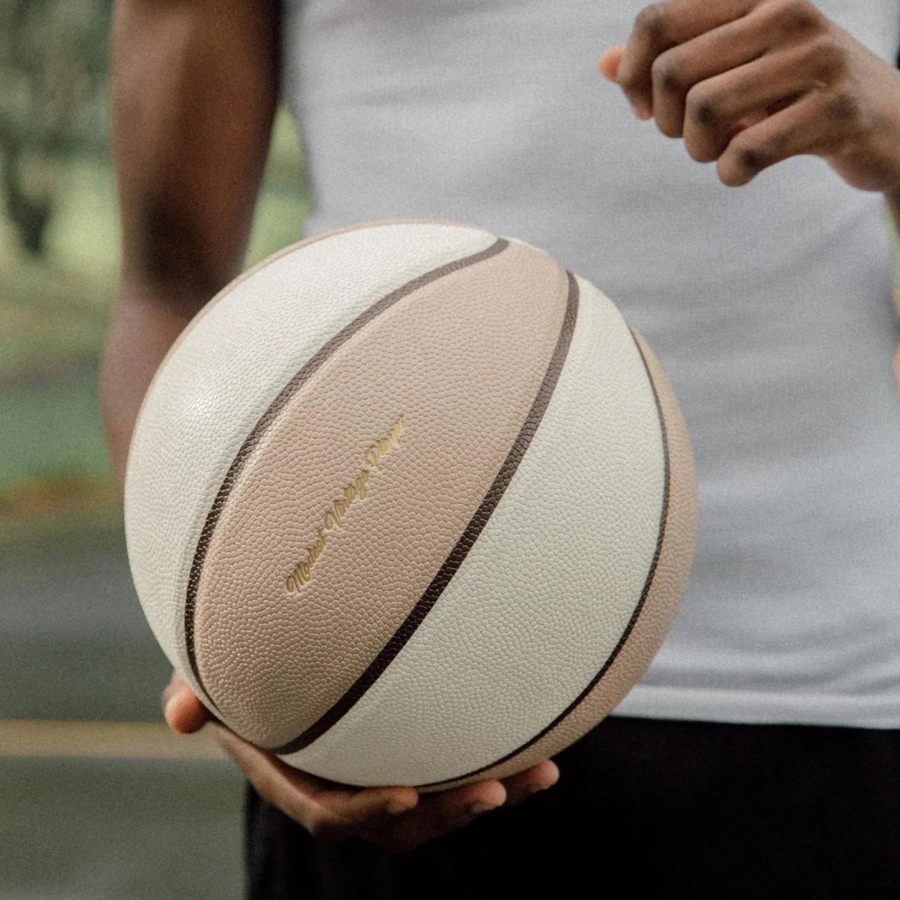 A man holding a leather basketball with beige and white panels, featuring a gold debossed logo on the top white panel.