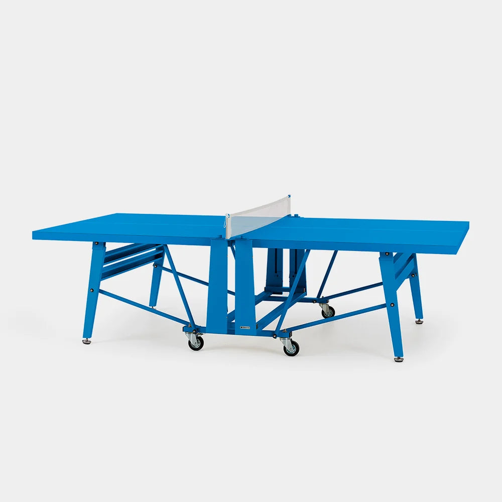 A bright blue convertible ping-pong table shown open, with a white net and black caster wheels, photographed on a clean light gray studio background.