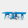A bright blue convertible ping-pong table shown open, with a white net and black caster wheels, photographed on a clean light gray studio background.