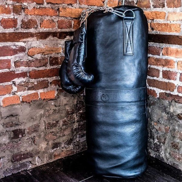 Black punching bag and gloves against a brick wall.