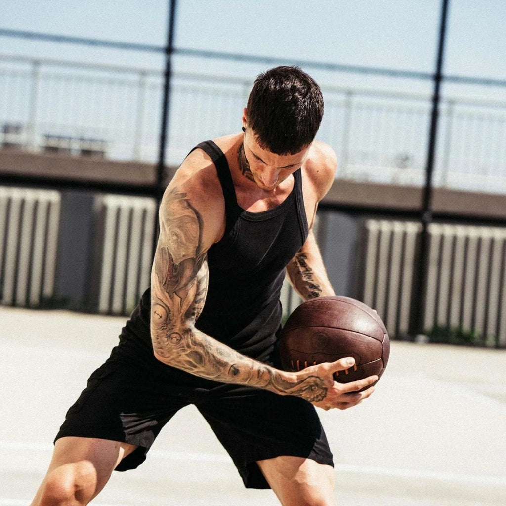 Man with tattoos holding a medicine ball on an outdoor court