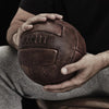 a man holding a vintage looking soccer ball with T-shaped panels.