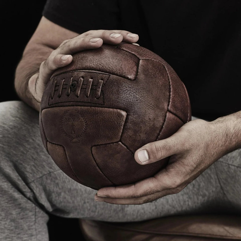 a man holding a vintage looking soccer ball with T-shaped panels.