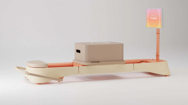 Connected Pilates reformer by Frame Fitness on a wooden base with pink accents and a frame holder.