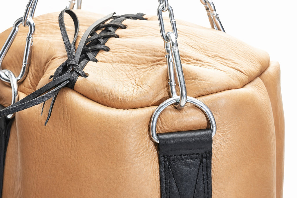 Close-up of a tan leather bag with black straps and metal hardware on a white background